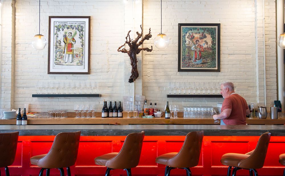 Empty bar with red counter, brown stools and vintage posters on white brick wall.