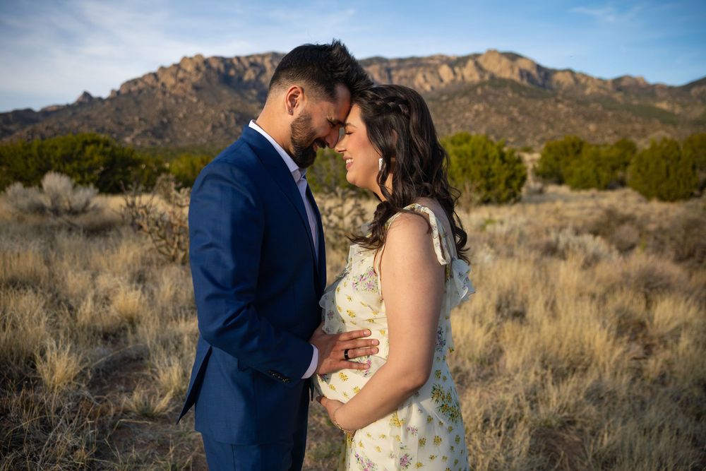 Couple sharing a romantic moment in a desert landscape with Sandia Mountains in the background during golden hour.