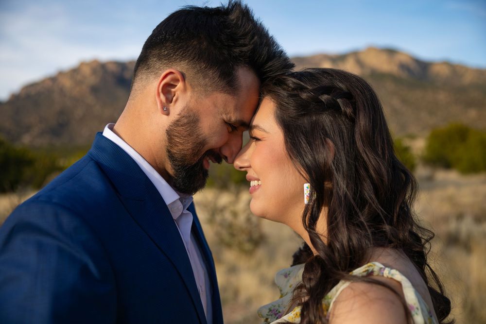 Couple sharing a romantic forehead touch outdoors with mountain landscape backdrop in golden hour light.