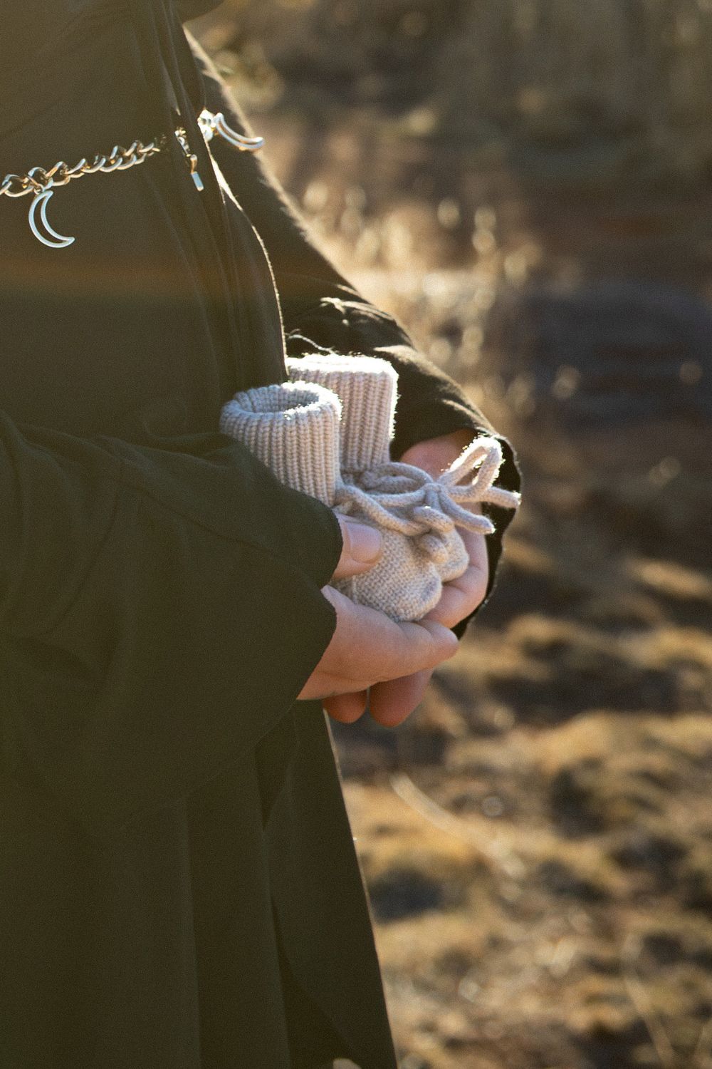 A close-up shot of tiny white baby booties being held against a dark background in natural light.