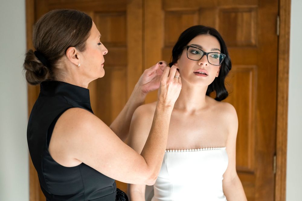 A bride and her bridesmaid share an emotional moment while getting ready in a rustic wooden room.