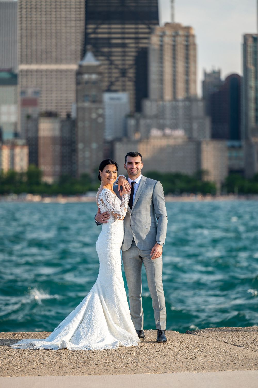 Newlywed couple poses on Lake Michigan shoreline with Chicago skyline in background during summer wedding photoshoot.