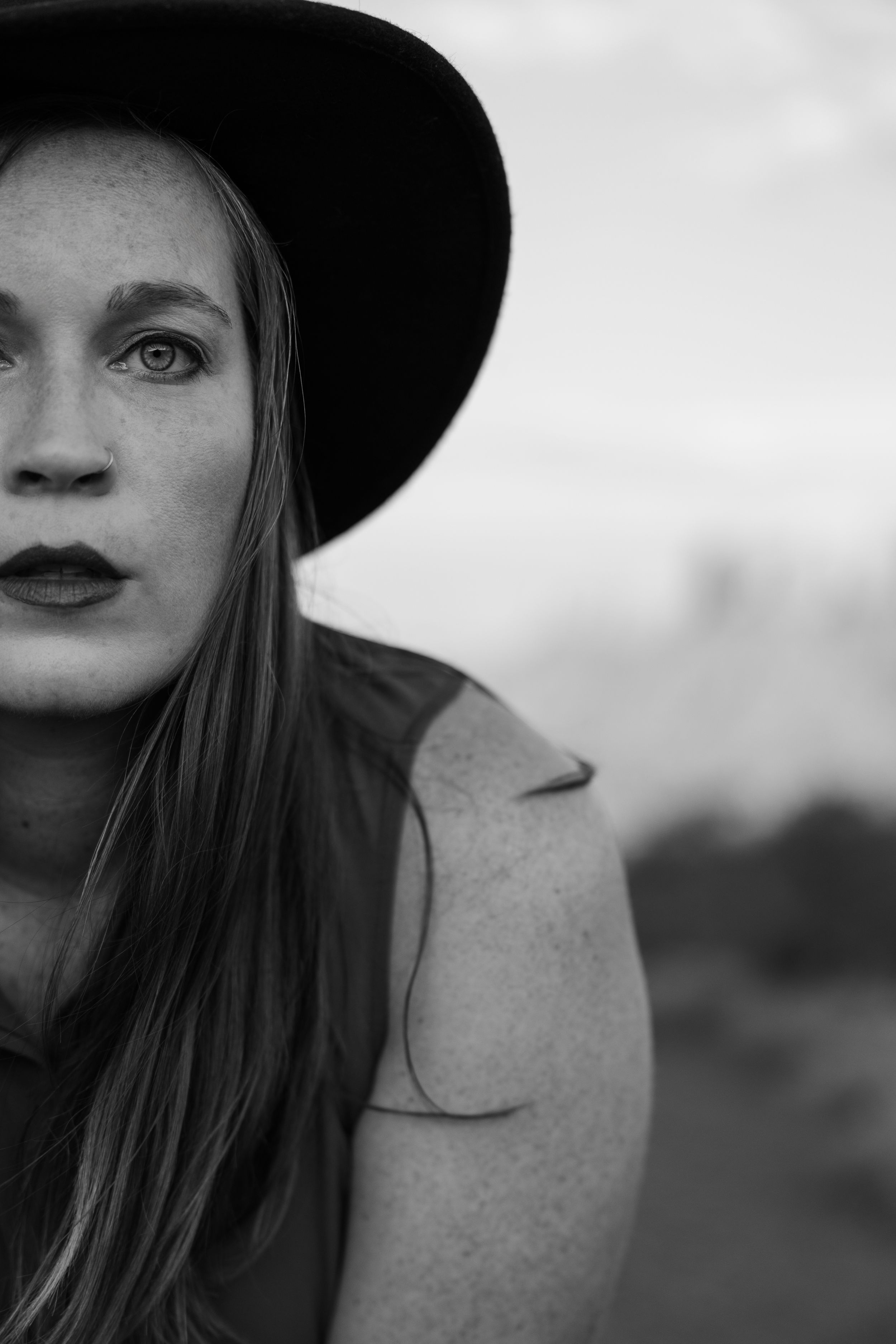 Artistic black and white portrait of someone wearing a wide-brimmed hat against a blurred background.