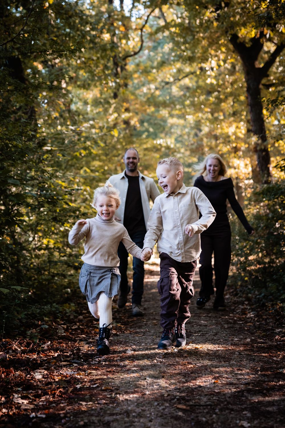 A joyful autumn scene shows people running through a wooded path with golden sunlight filtering through the trees.
