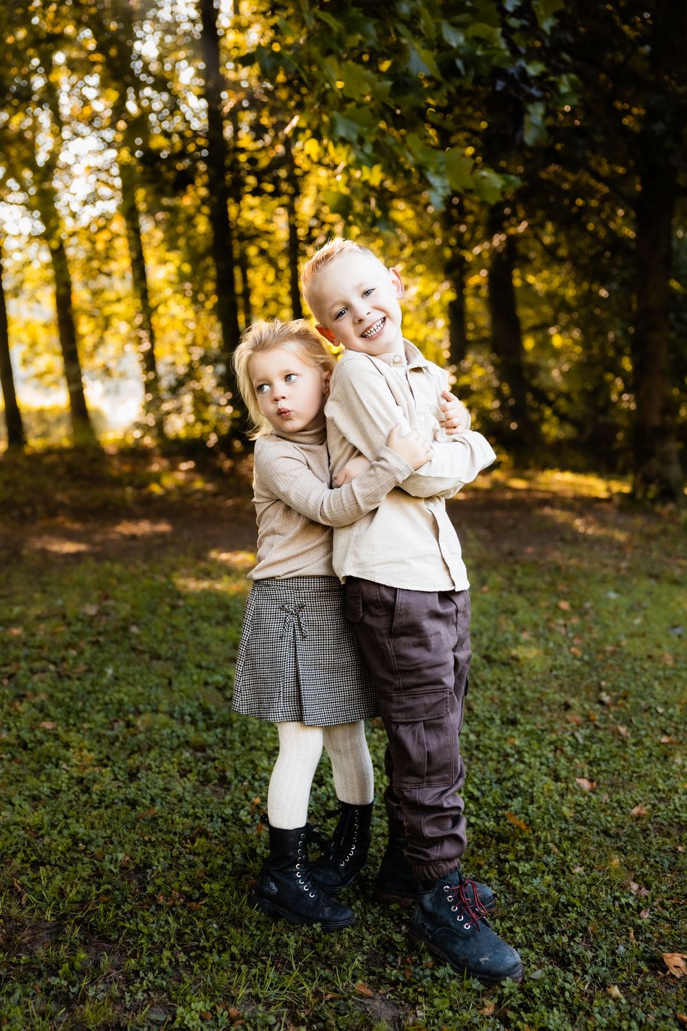Two children play and hug together in a sunlit autumn forest setting with golden light filtering through trees.