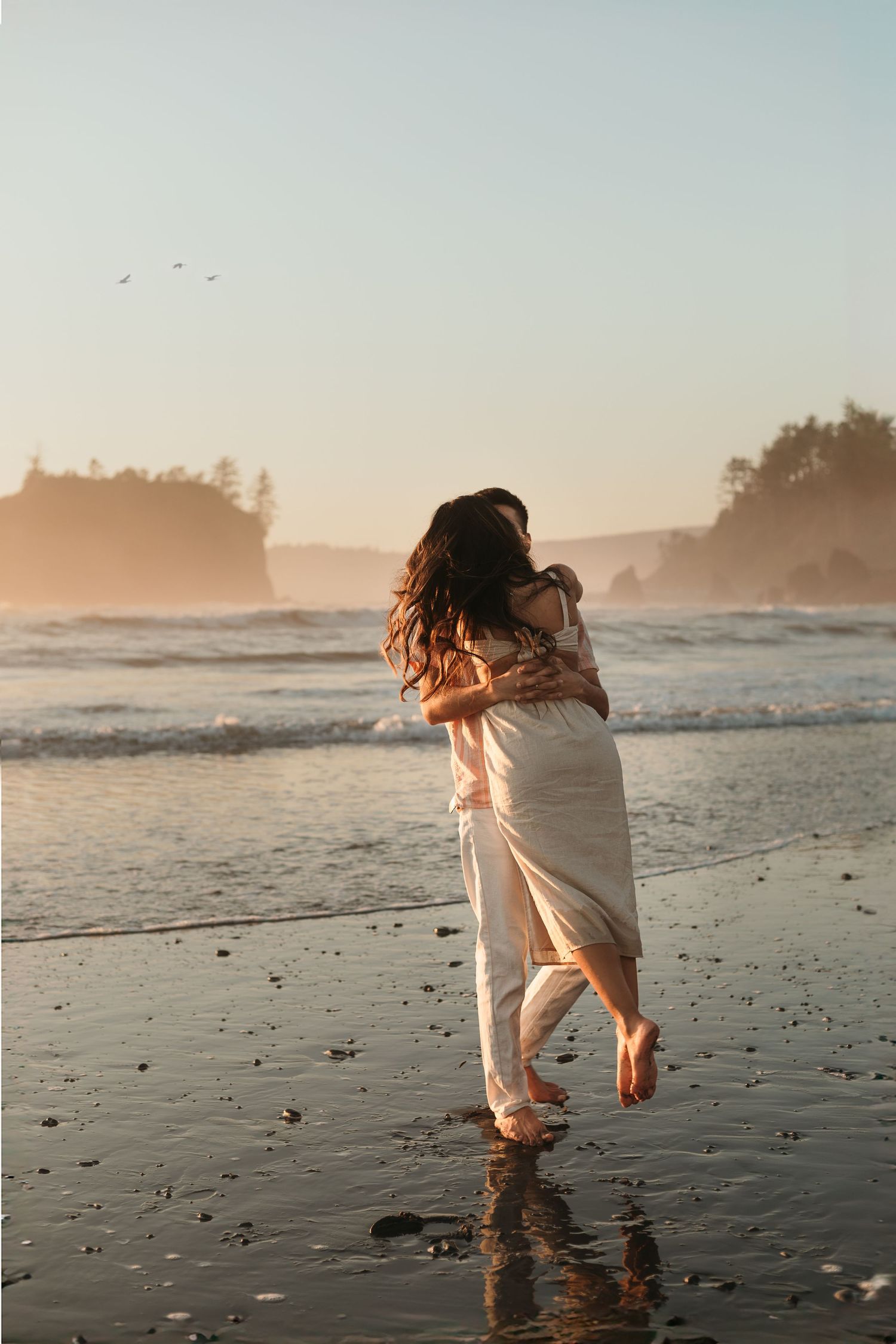 Couple twirls and plays in ocean waves in Washington