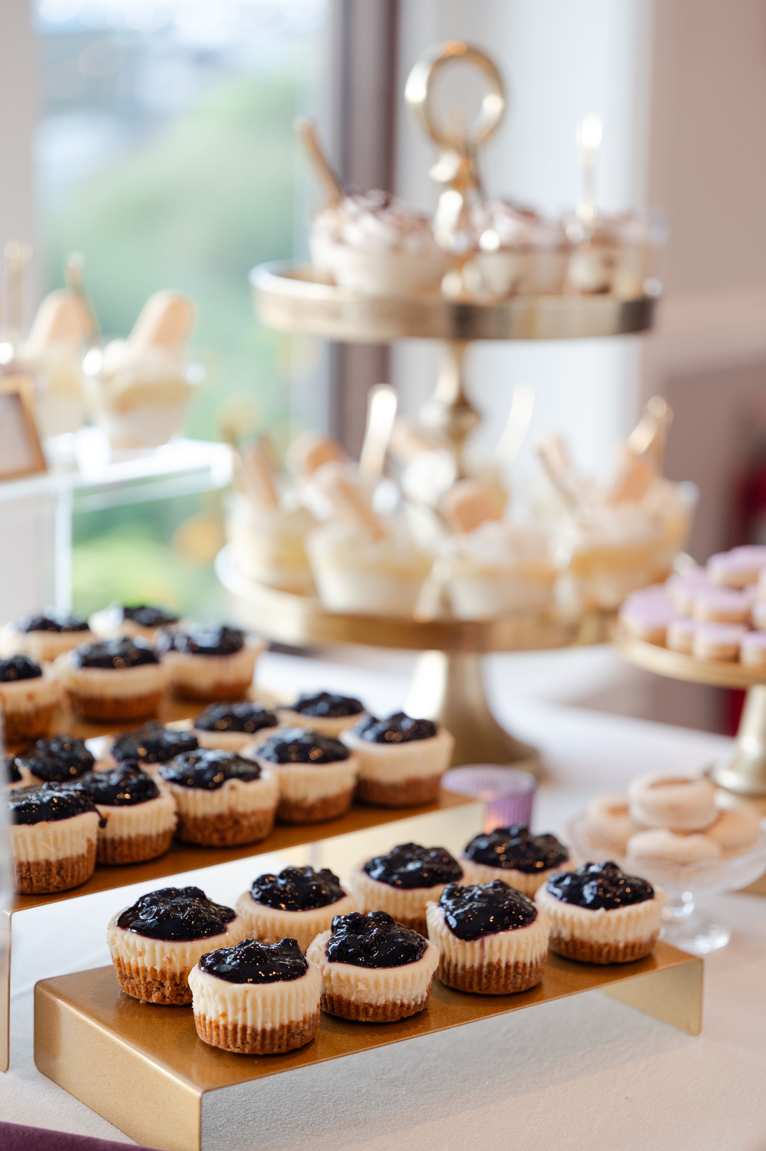 Mini chocolate cheesecakes with dark berry topping displayed on gold serving trays at an elegant dessert table.