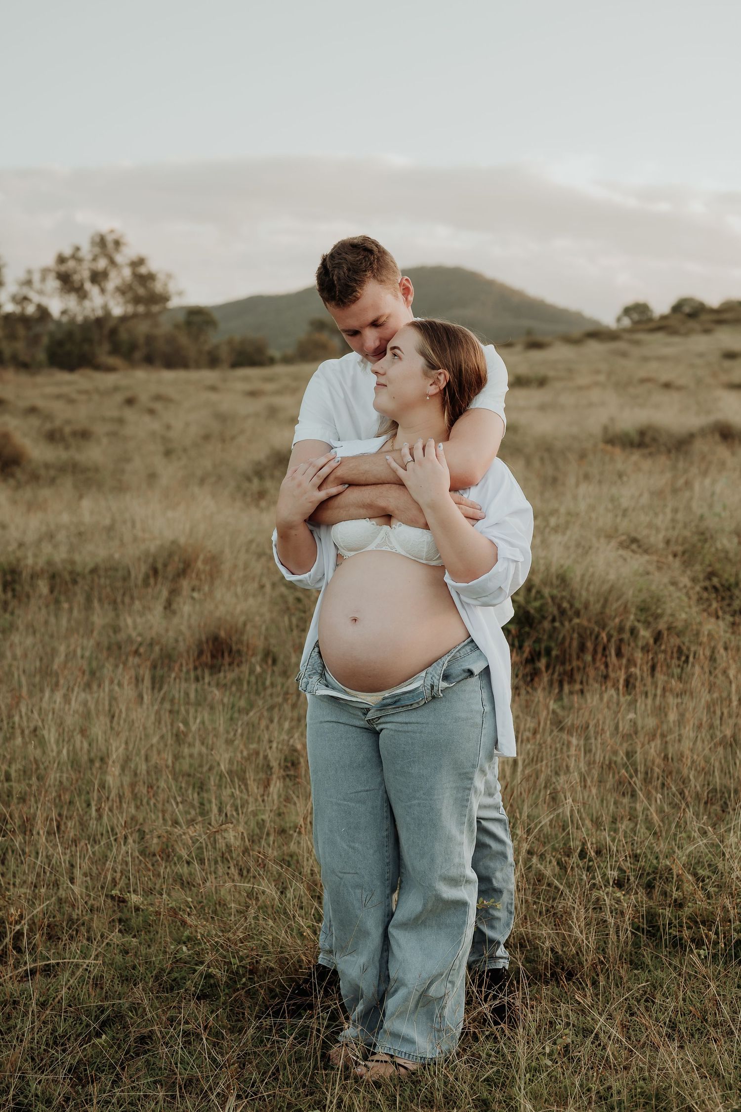 Artistic maternity photo showing pregnant belly with white lace robe in natural outdoor setting.
