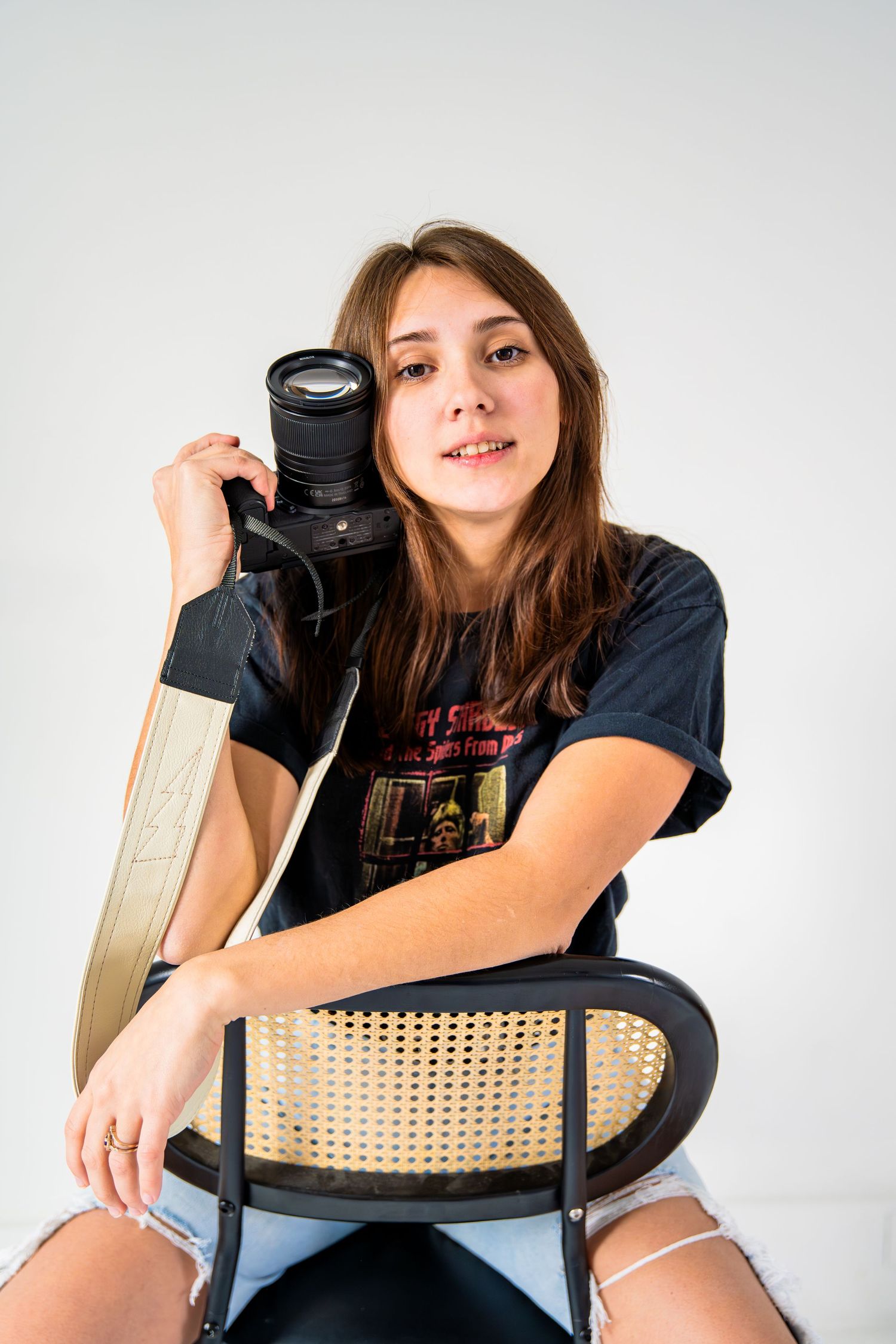 Khylianna Flowers of Flowers Photography Casual portrait of photographer with camera sitting on rattan chair against white background.