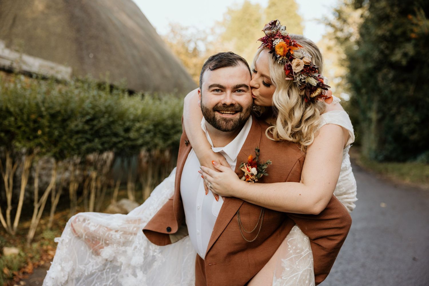 Romantic autumn wedding portrait in front of thatched cottage with couple embracing.