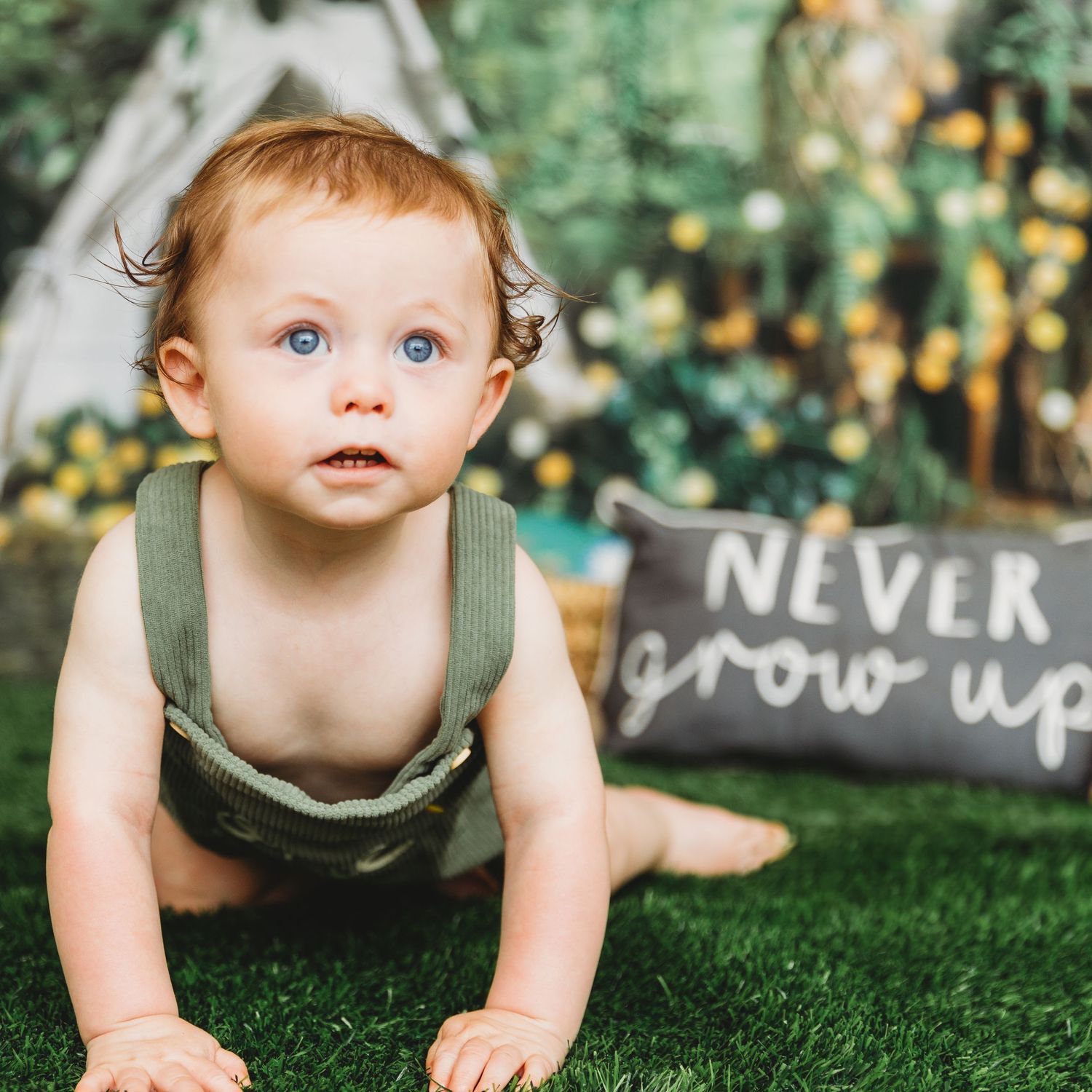 Baby crawling on grass with decorative text signs in background during outdoor photoshoot.