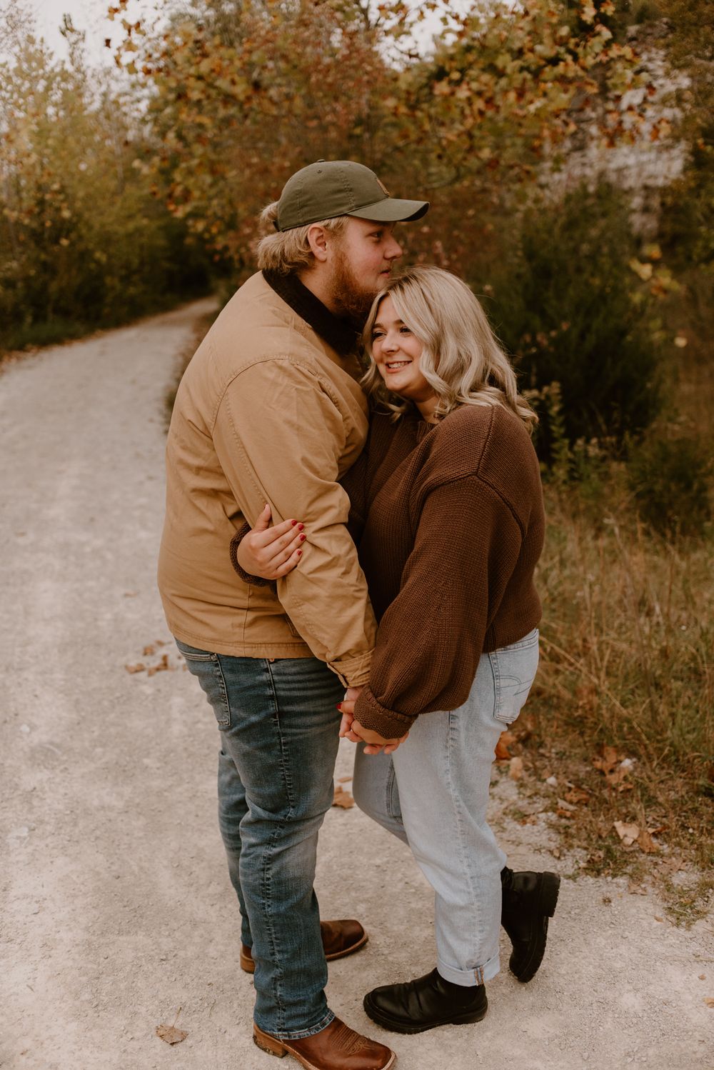 Playful couple in coordinating brown outfits sharing laughs on a gravel path.