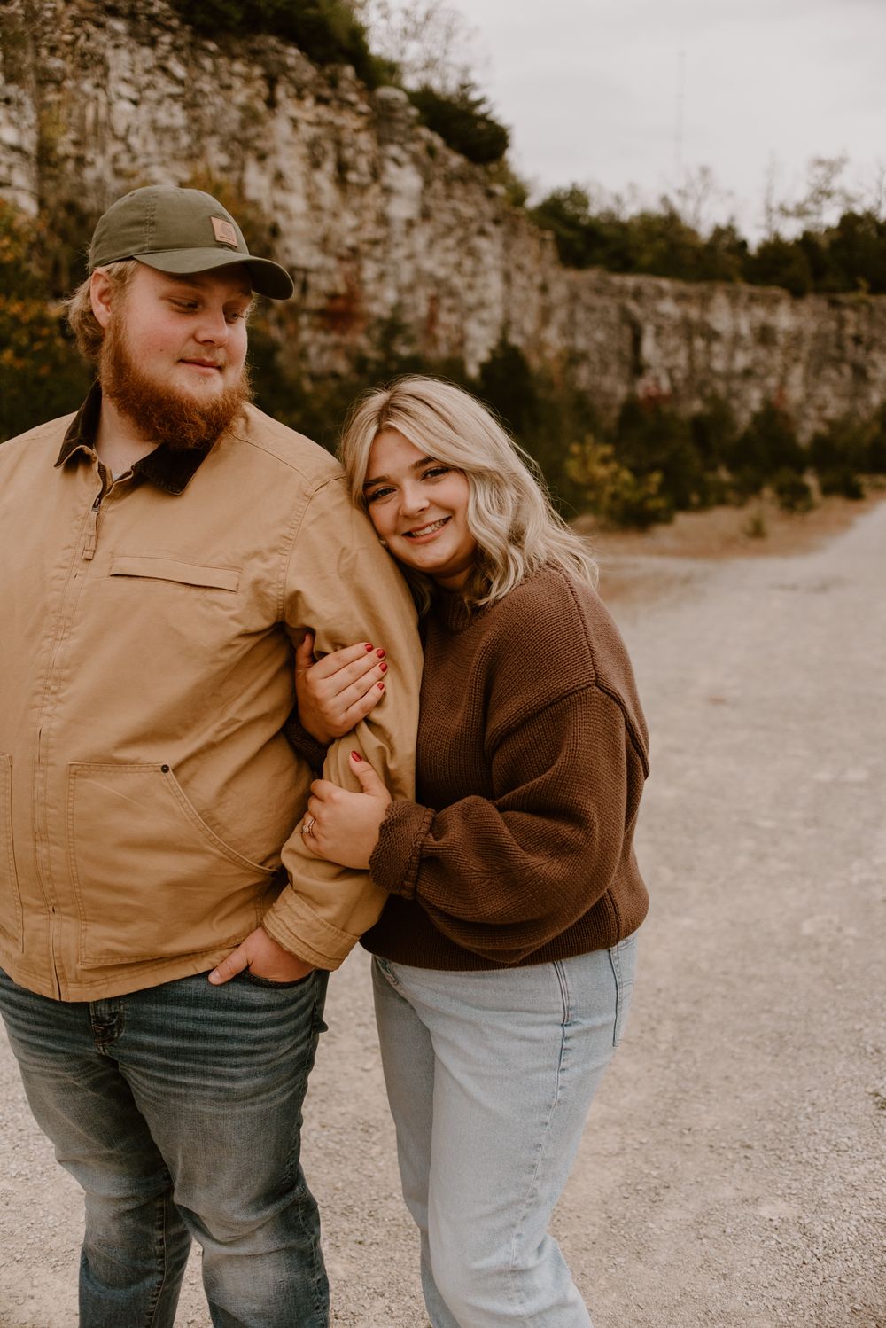 Couple in casual fall outfits sharing intimate moments on a gravel path near rocky cliffs.