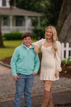 A pair stands together outdoors in coordinating outfits of mint green and cream against a blurred natural background.