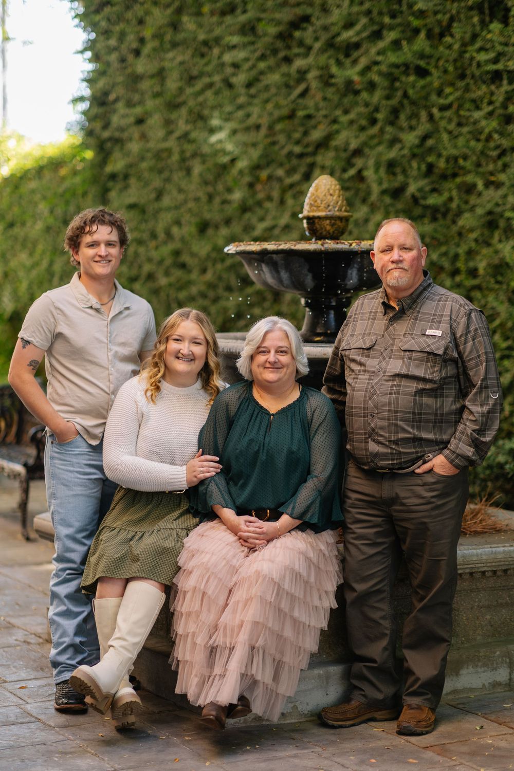 Family portrait series taken outdoors against a green hedge background with soft evening lighting.