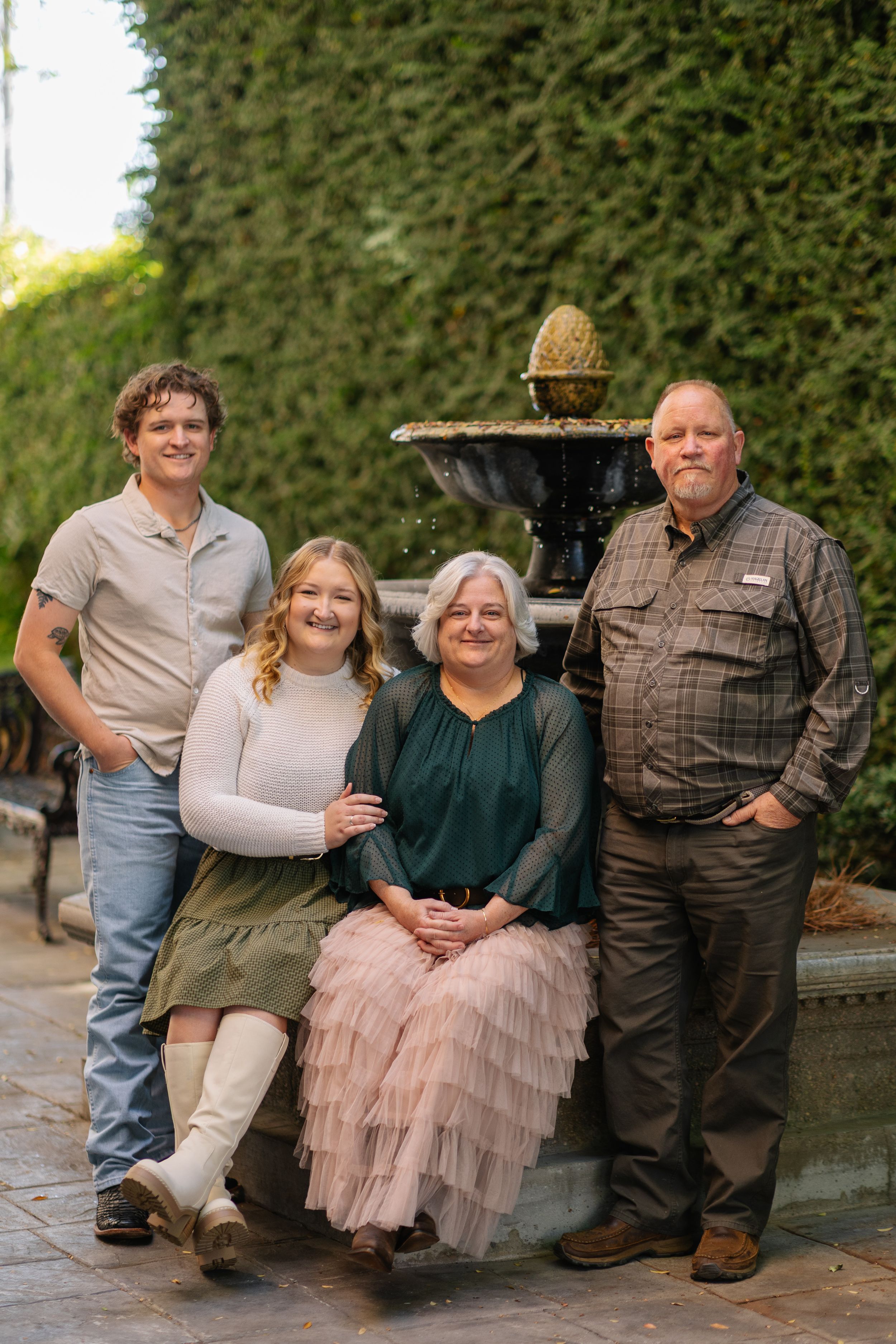 Family portrait series taken outdoors against a green hedge background with soft evening lighting.
