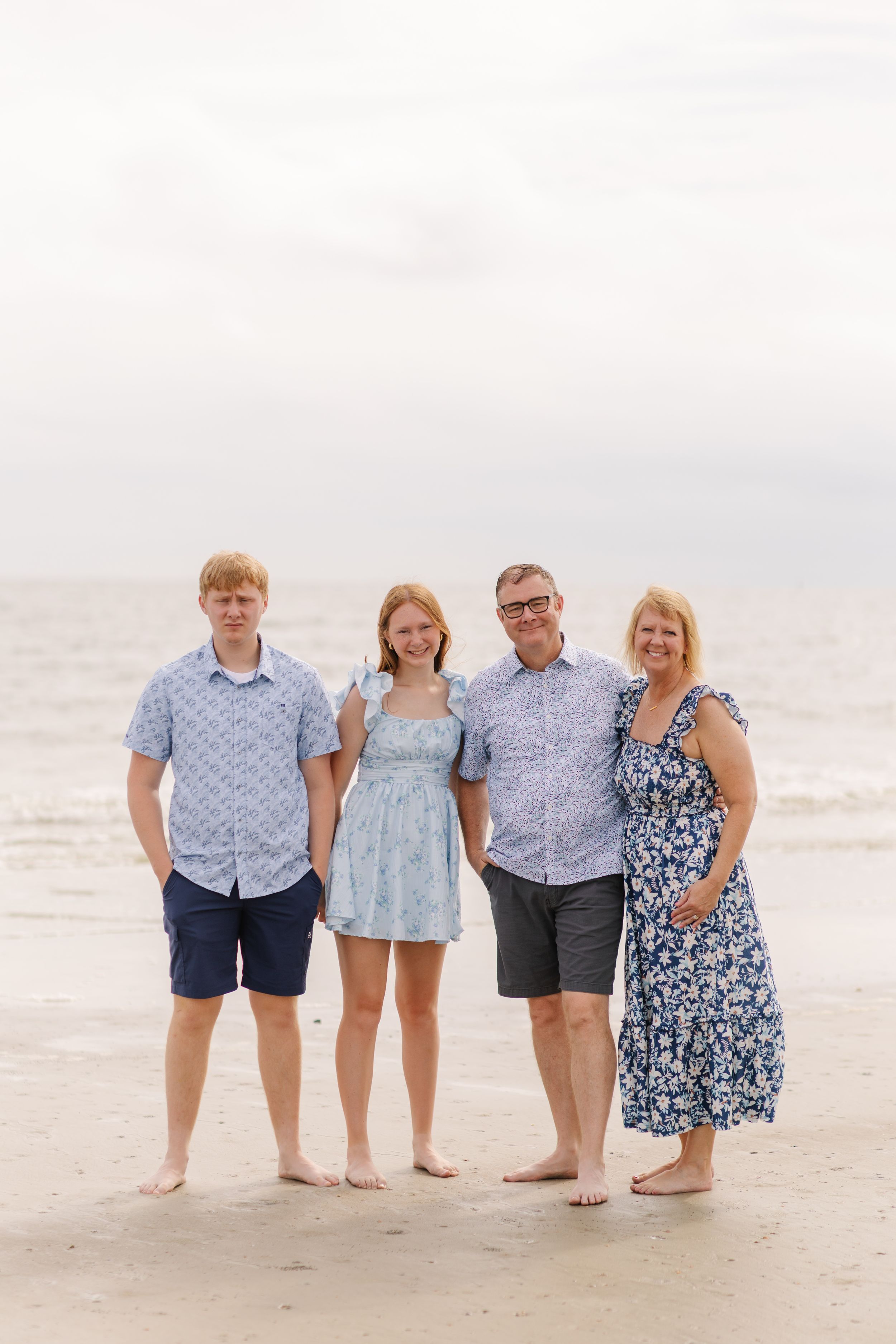 Four people stand together on a sandy beach at sunset wearing coordinated blue and white outfits.