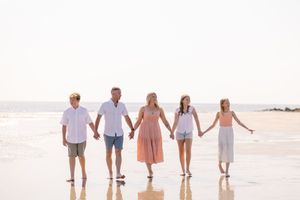 A group of people holding hands while walking along the beach at sunset with ocean waves in the background.