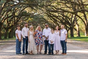 A group of people in coordinating white and blue outfits pose together for outdoor family photos under oak trees.