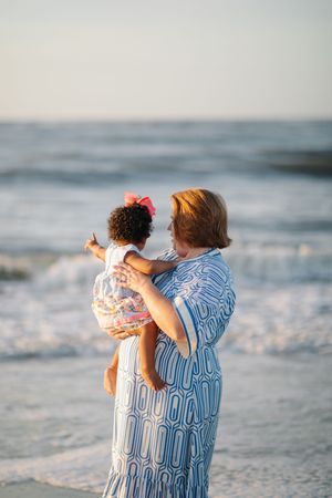 Two people in matching striped outfits embrace while standing on a beach at sunset with ocean waves in the background.