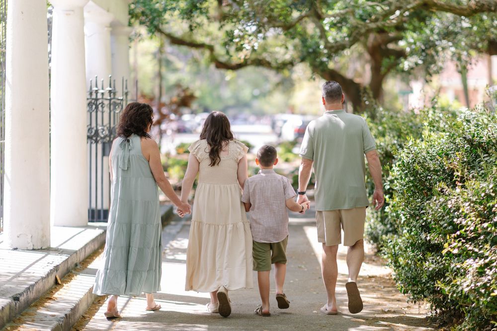 Family of four walking hand-in-hand down a tree-lined sidewalk in Savannah, GA.