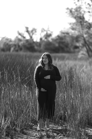 Black and white photo of a person in dark clothing sitting in a tall grass field.