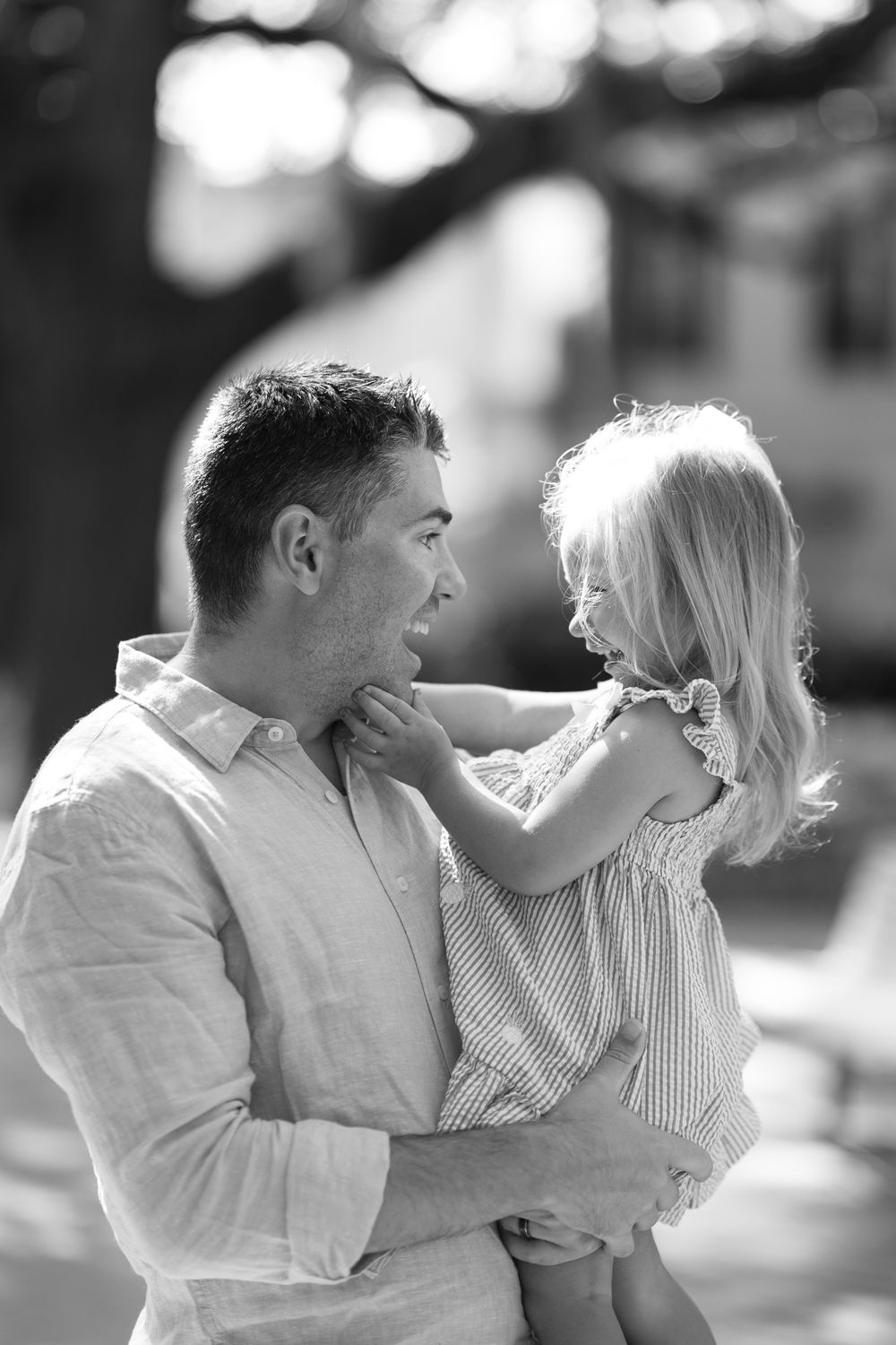 Black and white photo of a father holding his young blonde daughter outdoors, sharing a joyful moment.