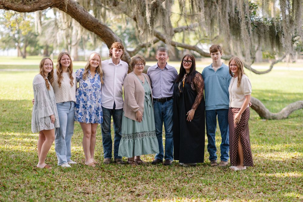 Large family group portrait outdoors under mossy oak trees on green lawn, smiling together for a professional photo.