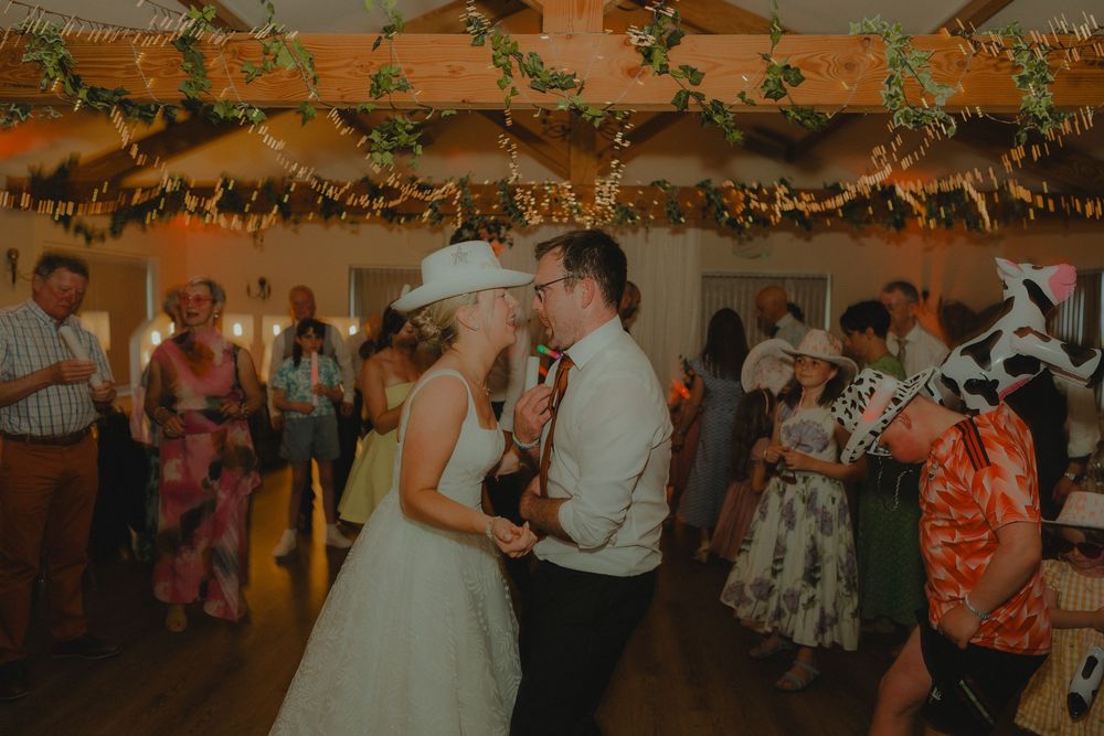 Bride and groom share first dance at rustic wedding reception with string lights and greenery decorations.