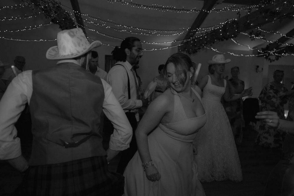Black and white wedding reception photo of guests dancing joyfully under twinkling fairy lights.