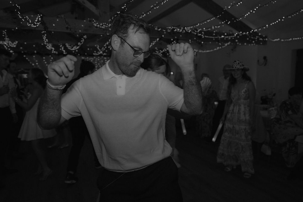 Man dancing energetically at a party in black and white photo with festive lights in background.