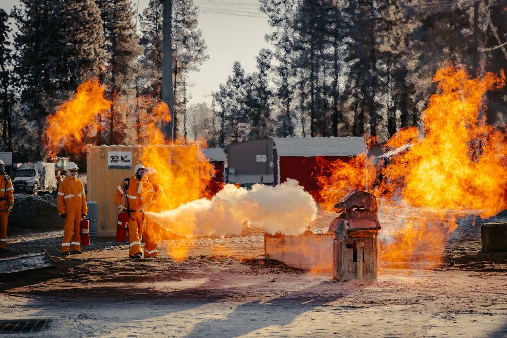 Firefighters in orange gear on a fire while conducting gas service testing with fire extinguishers.