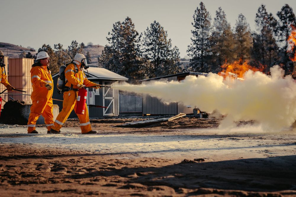 Firefighters in orange uniforms extinguishing flames during gas service testing using fire extinguishers.