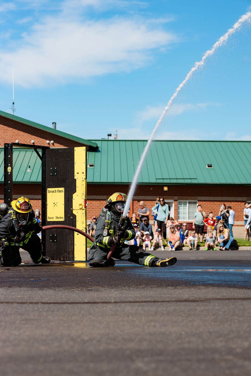 Firefighters extinguish a car fire with hoses at the annual fireman's festival, showcasing their skills and dedication.