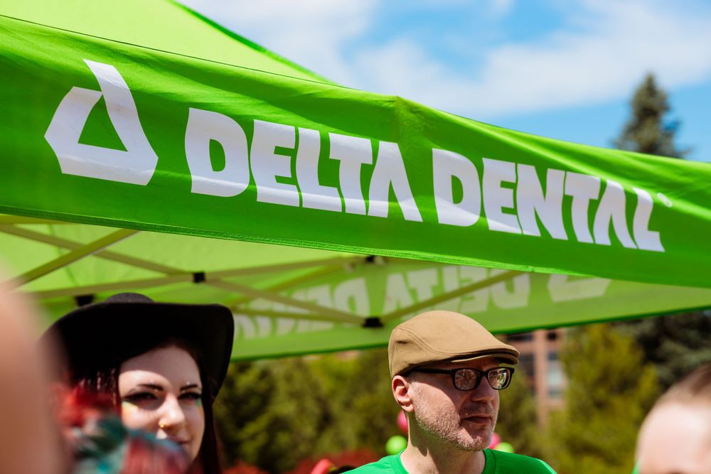 A diverse group of individuals gathered under a green Delta Dental tent, engaged in conversation and enjoying the outdoor setting.
