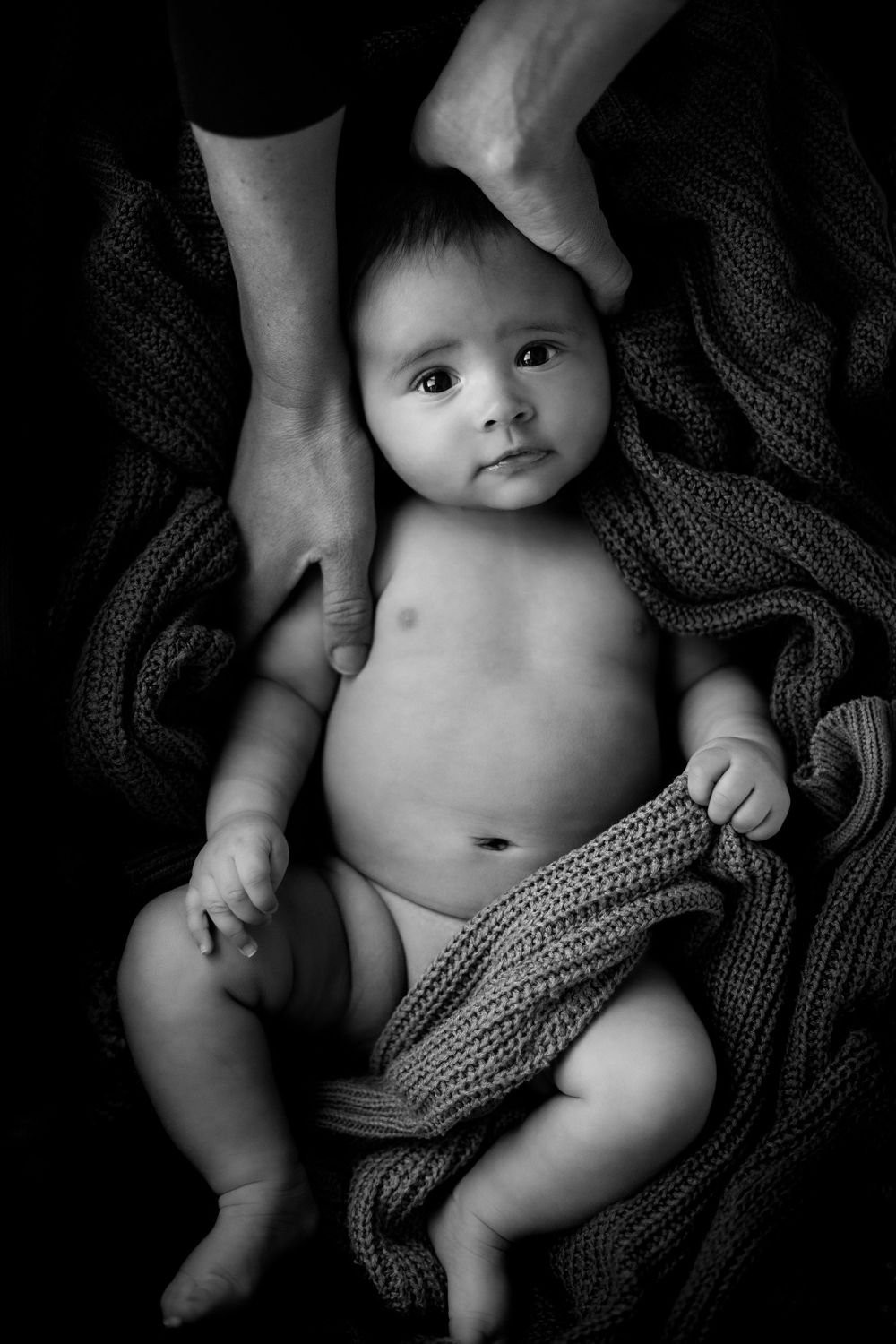 A black and white series of newborn baby portraits shows a small infant nestled in cozy knitted blankets.