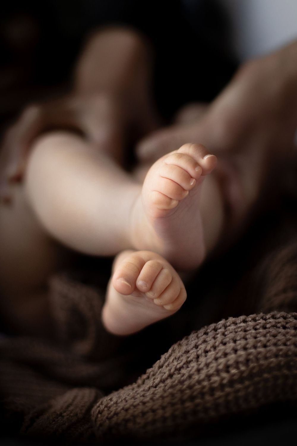 Close-up photo of tiny baby feet resting on a knit blanket with soft lighting and shallow depth of field.