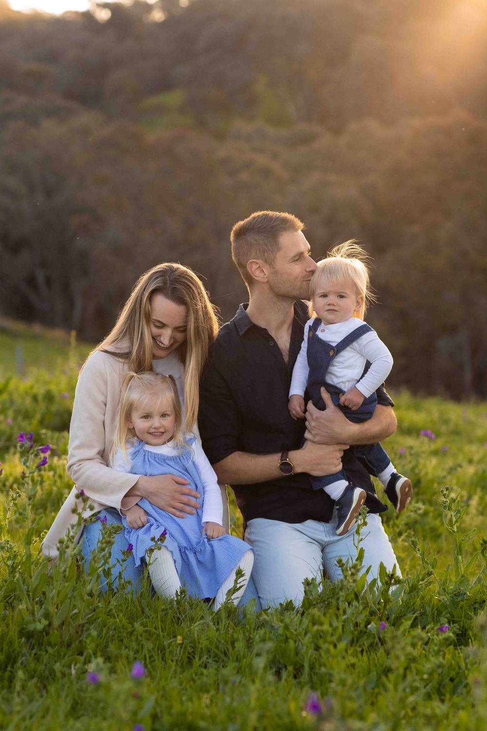 Family sitting together in a grassy meadow at sunset enjoying tender moments in nature.