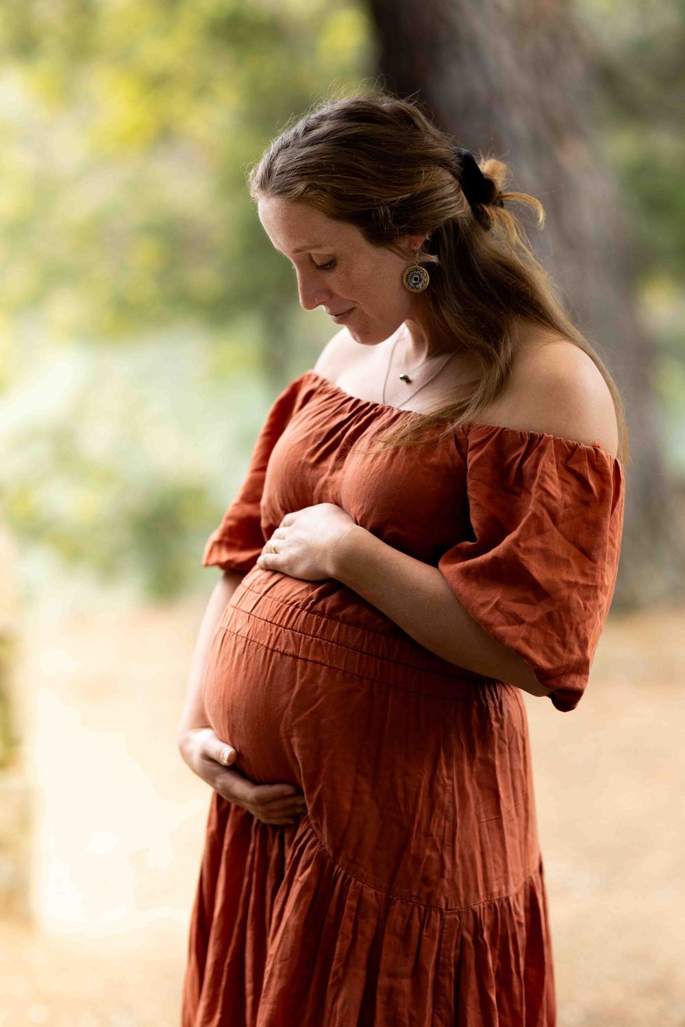 A person in a rust-colored dress cradles their pregnant belly in a series of outdoor maternity photos.
