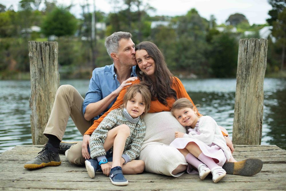 Family relaxes together on wooden dock by lake during sunset photo session.