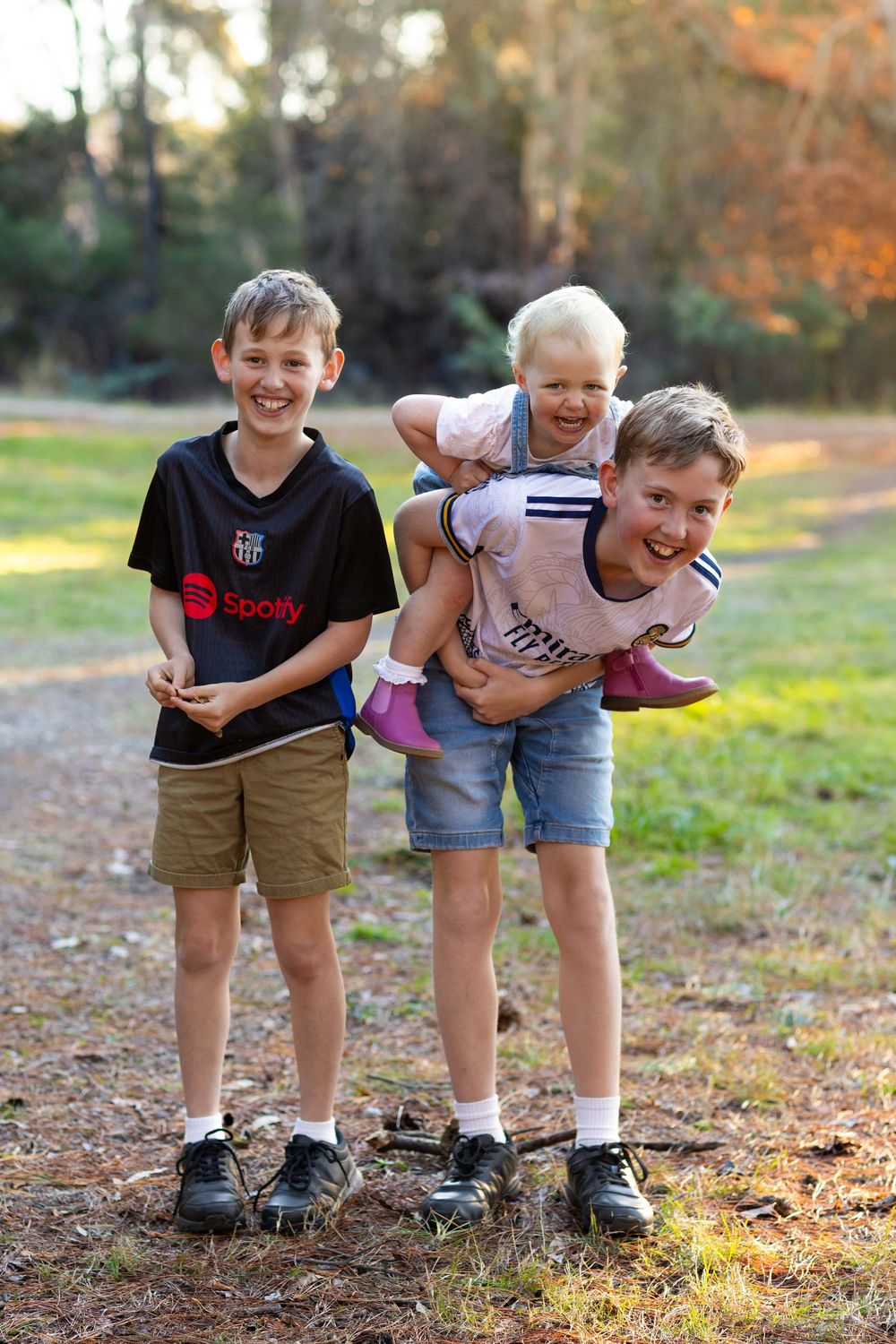 Three children playing and laughing together outdoors on an autumn day with fall foliage in the background.