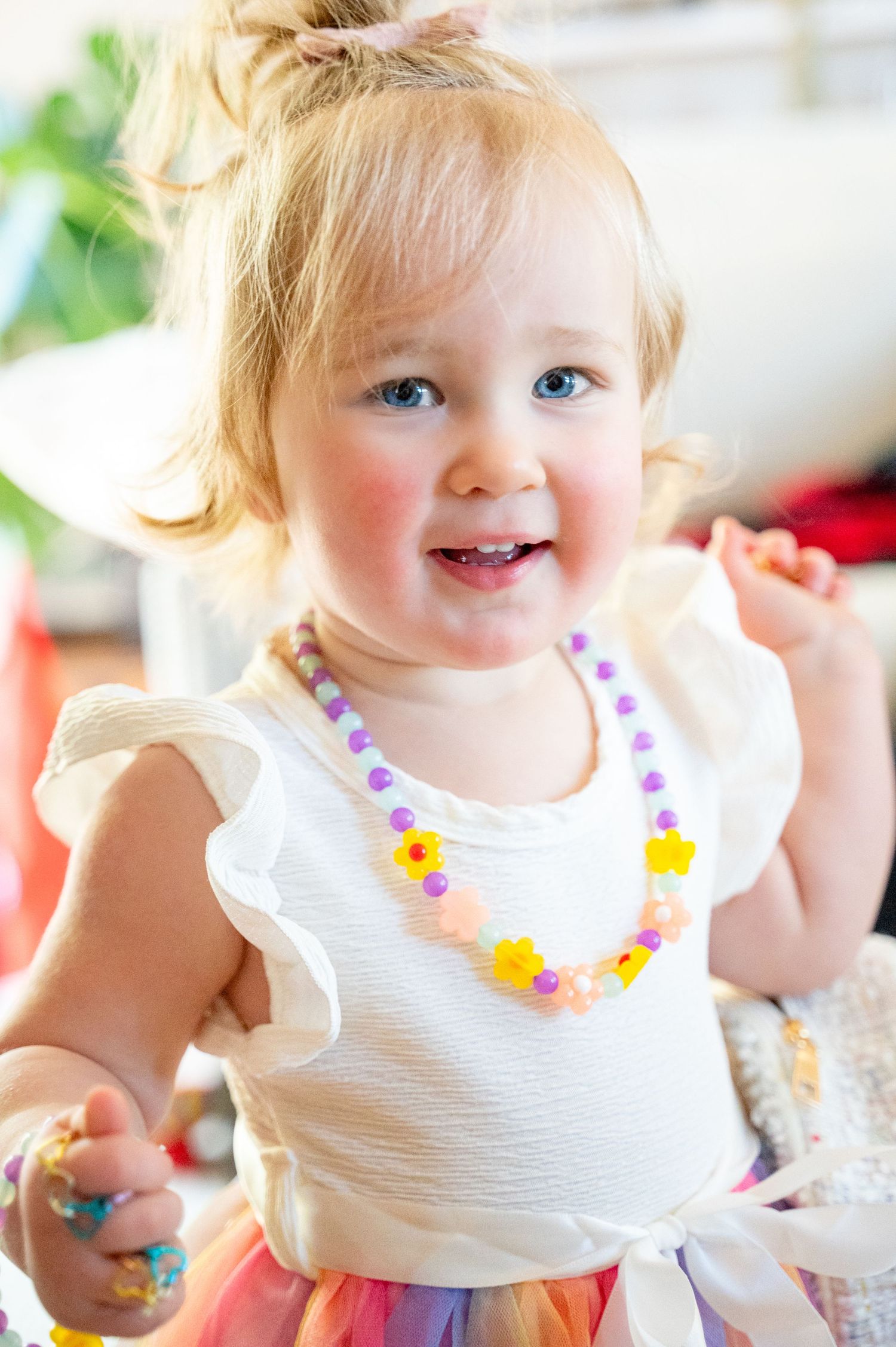 An adorable little girl with a precious smile, and a daisy necklace.  Smiling at the camera with sparkling blue eyes.