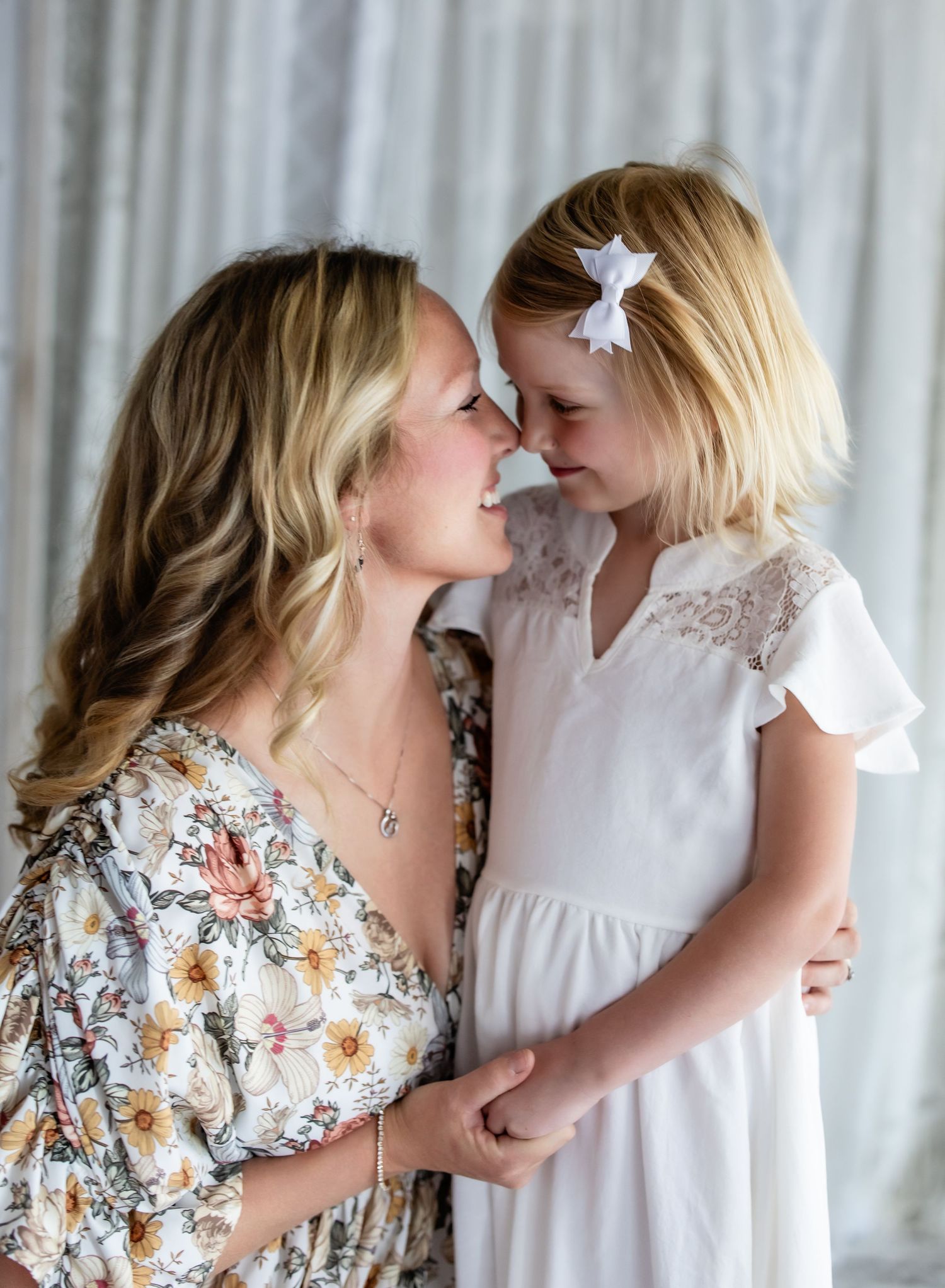 A tender moment between two people wearing floral and white dresses as they share a close embrace against a light backdrop.