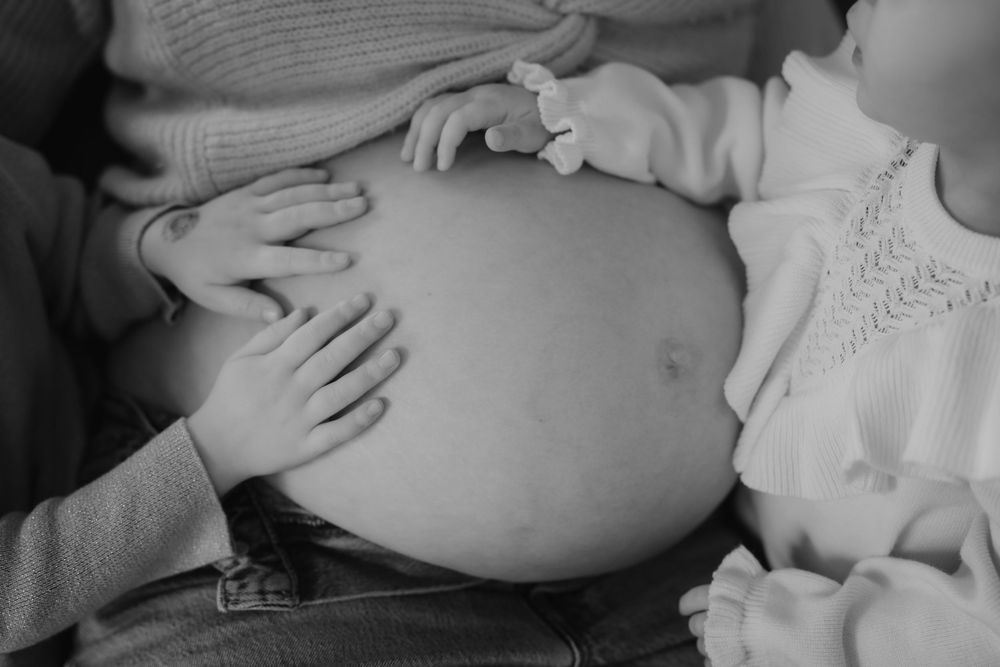 Multiple hands rest gently on a pregnant belly in an intimate black and white photograph.