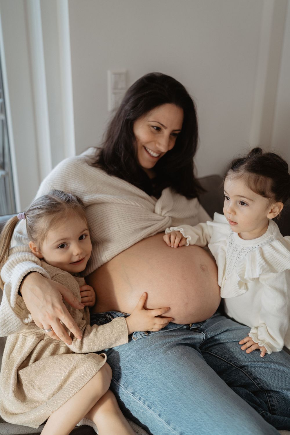 A tender moment between mother and child lying together on a couch in casual attire of beige sweater and jeans.