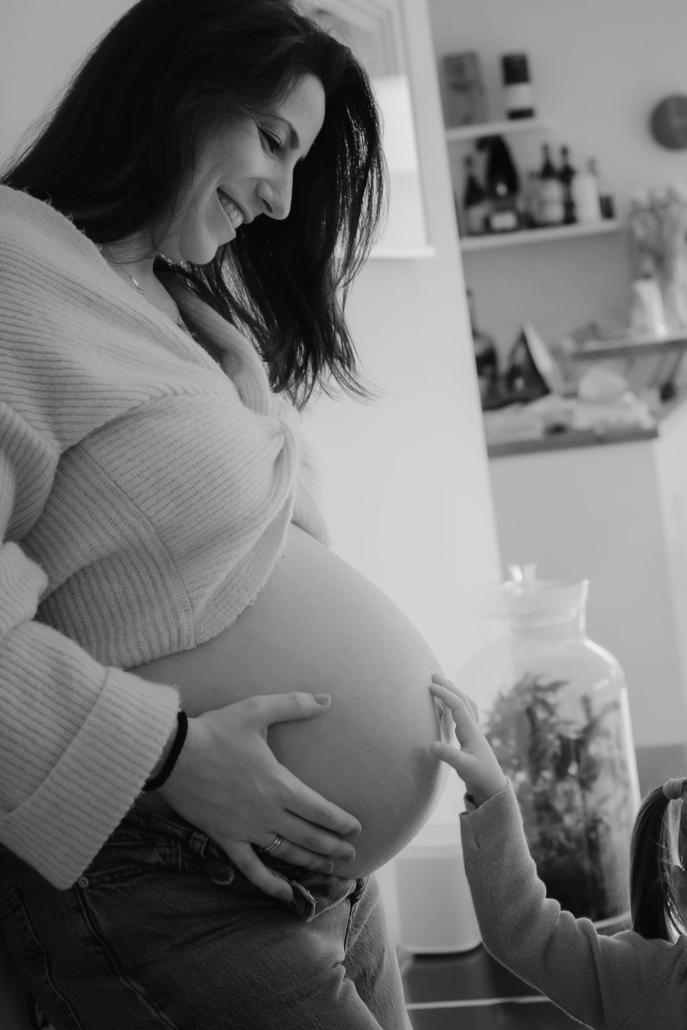 A pregnant woman in a white sweater holds her belly in a series of black and white maternity photos.
