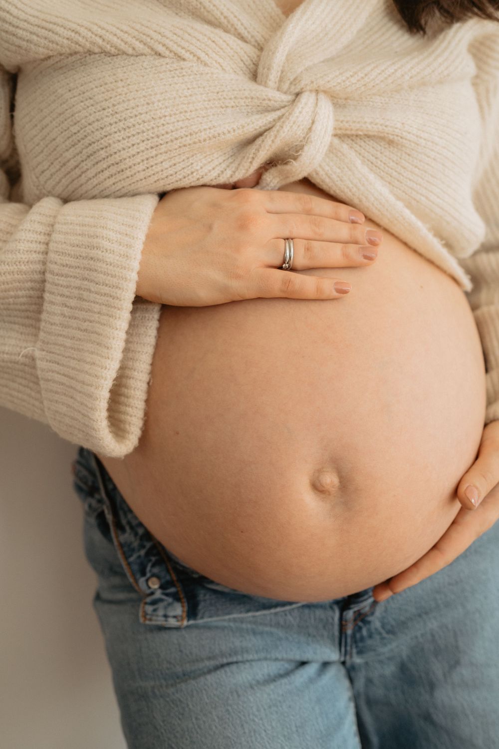 Close-up series of a pregnant belly in jeans and cream sweater showing progression of pregnancy growth.