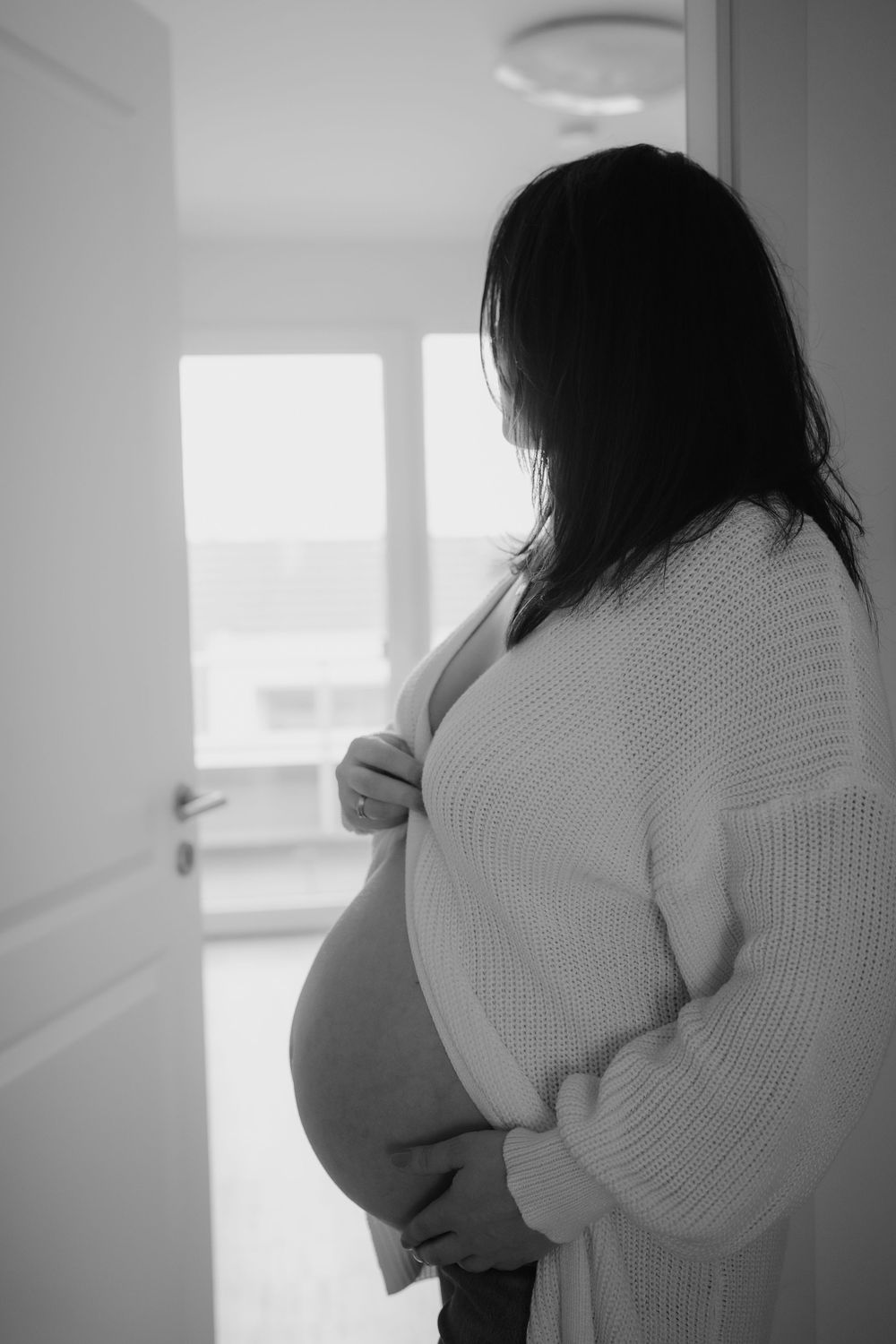Black and white profile series showing silhouette of pregnant woman in white knit sweater against window light.