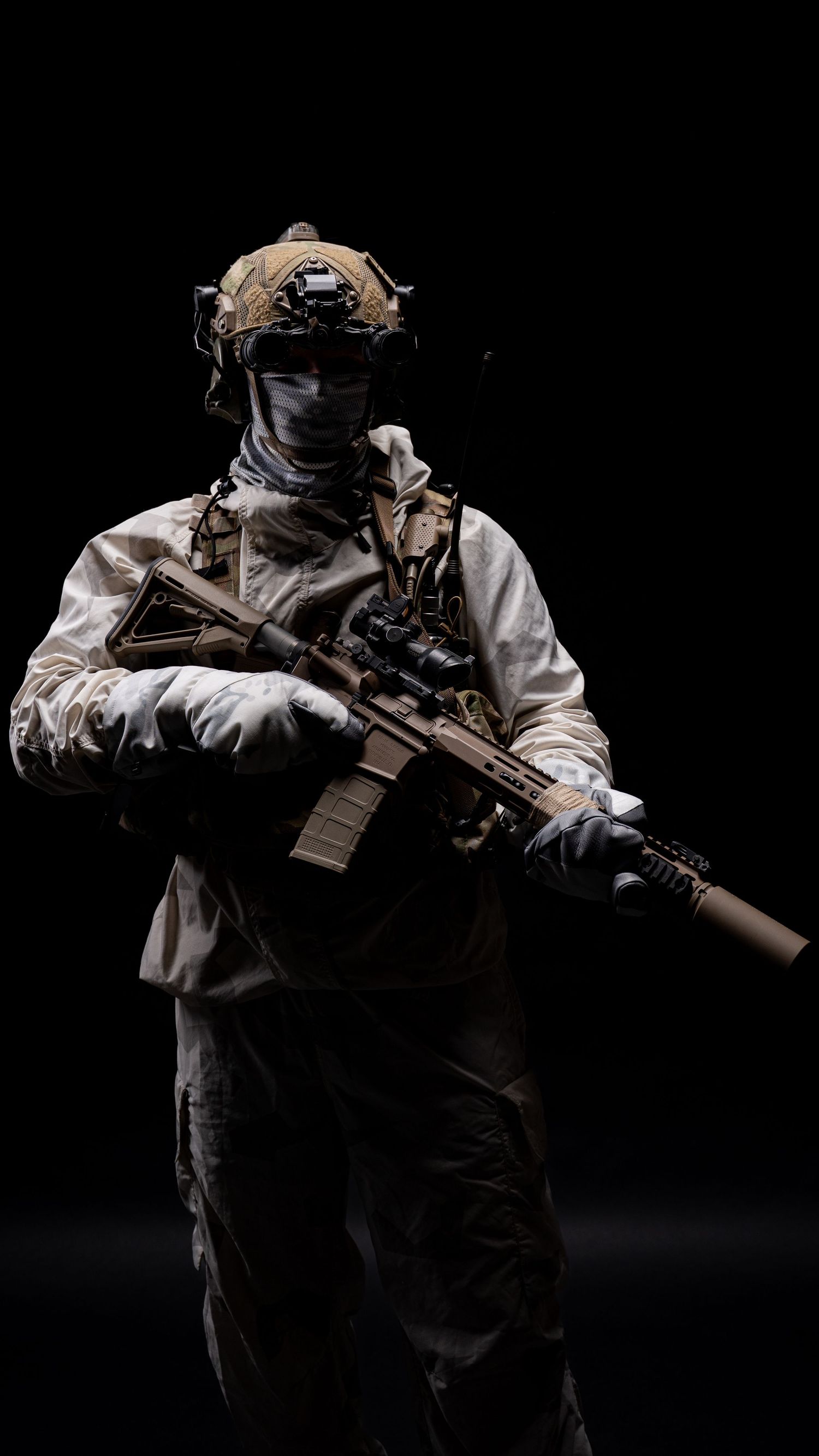 Military operator in tactical gear stands in shadows holding rifle with camouflage helmet and plate carrier visible.