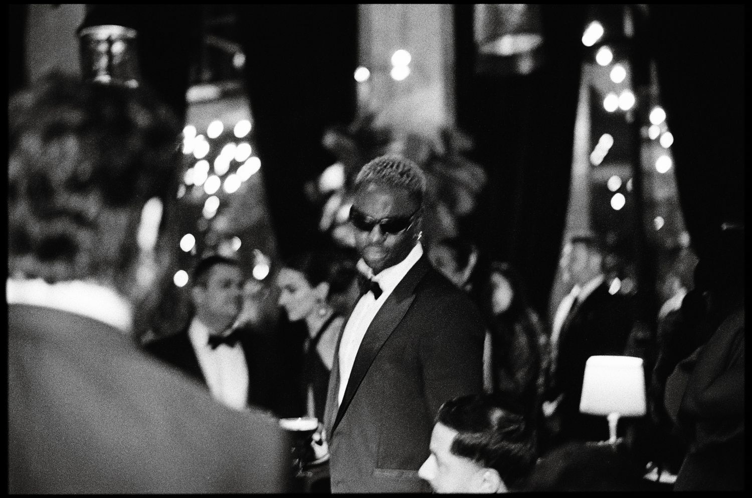 Elegant formal event guests in tuxedos mingling at a nighttime gathering.